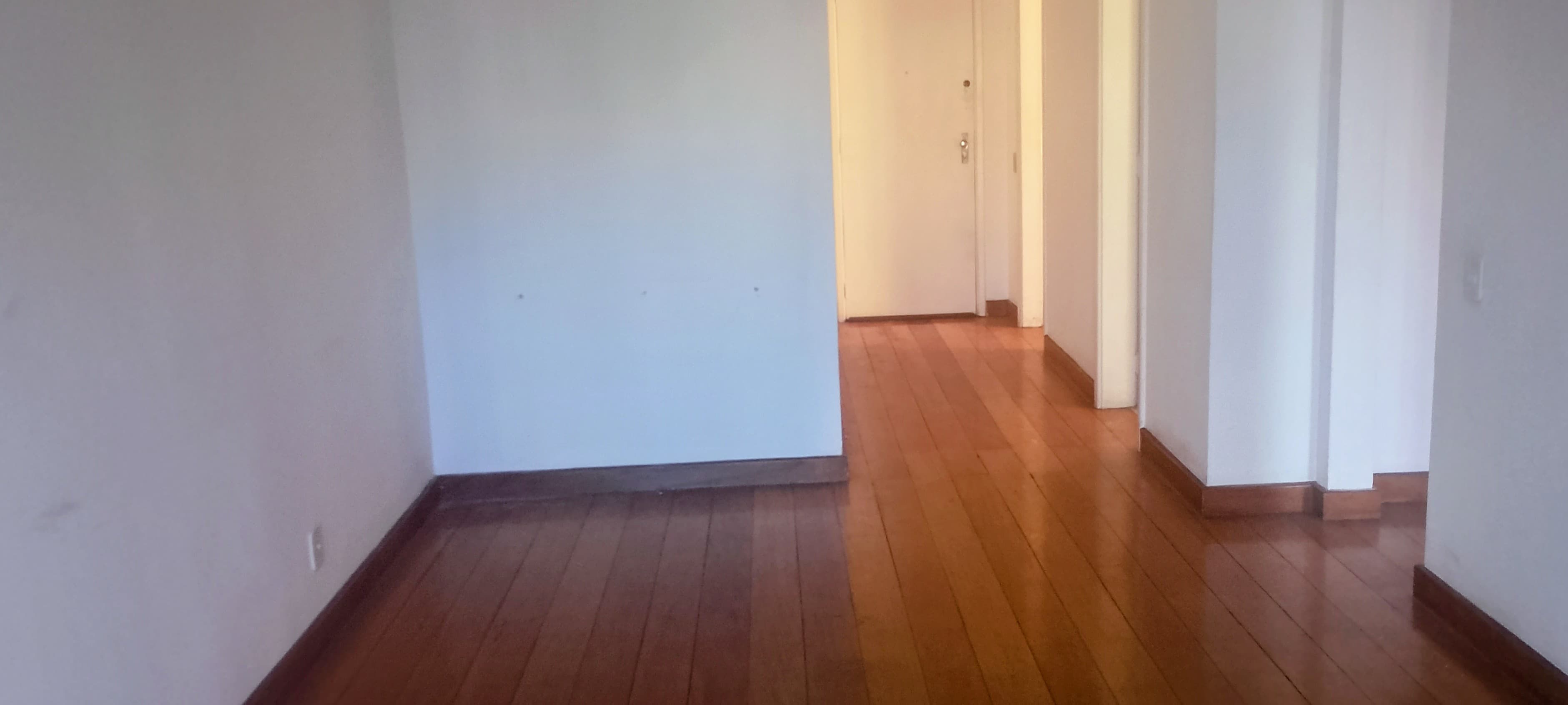 Ambiente interno com piso de madeira e paredes brancas, com porta ao fundo.