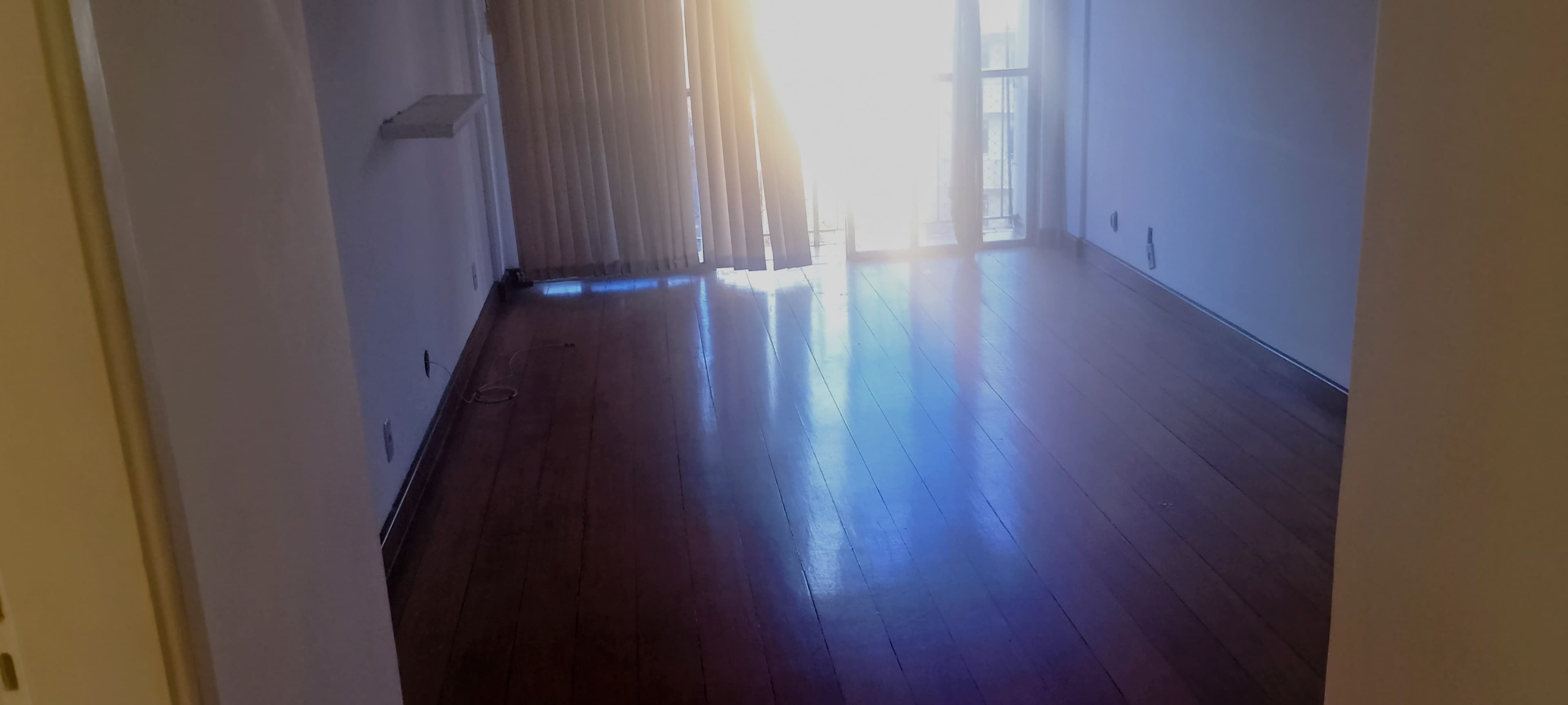 Sala com piso de madeira e acesso à varanda com cortina persiana.