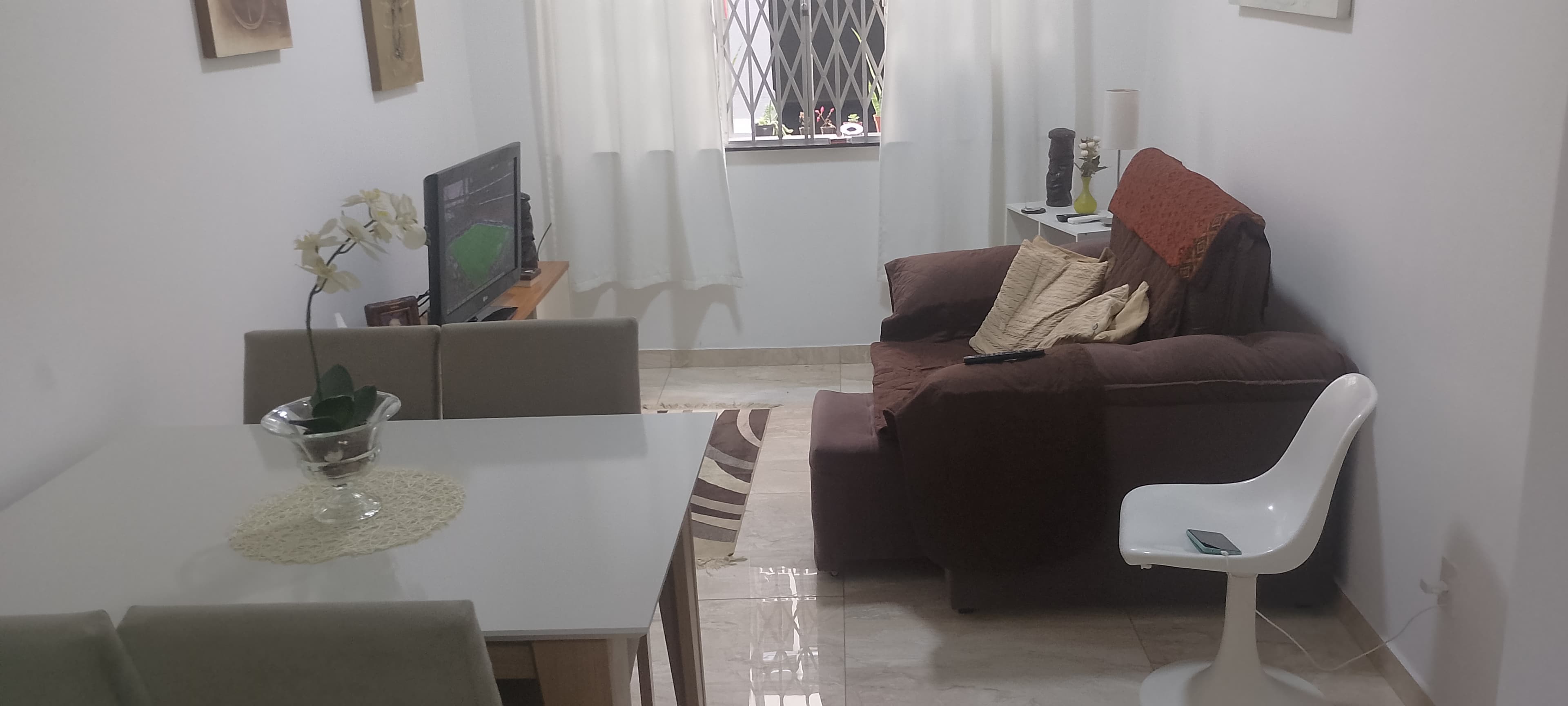 Sala de estar e jantar integrada com mesa, cadeiras, sofá marrom e televisão.