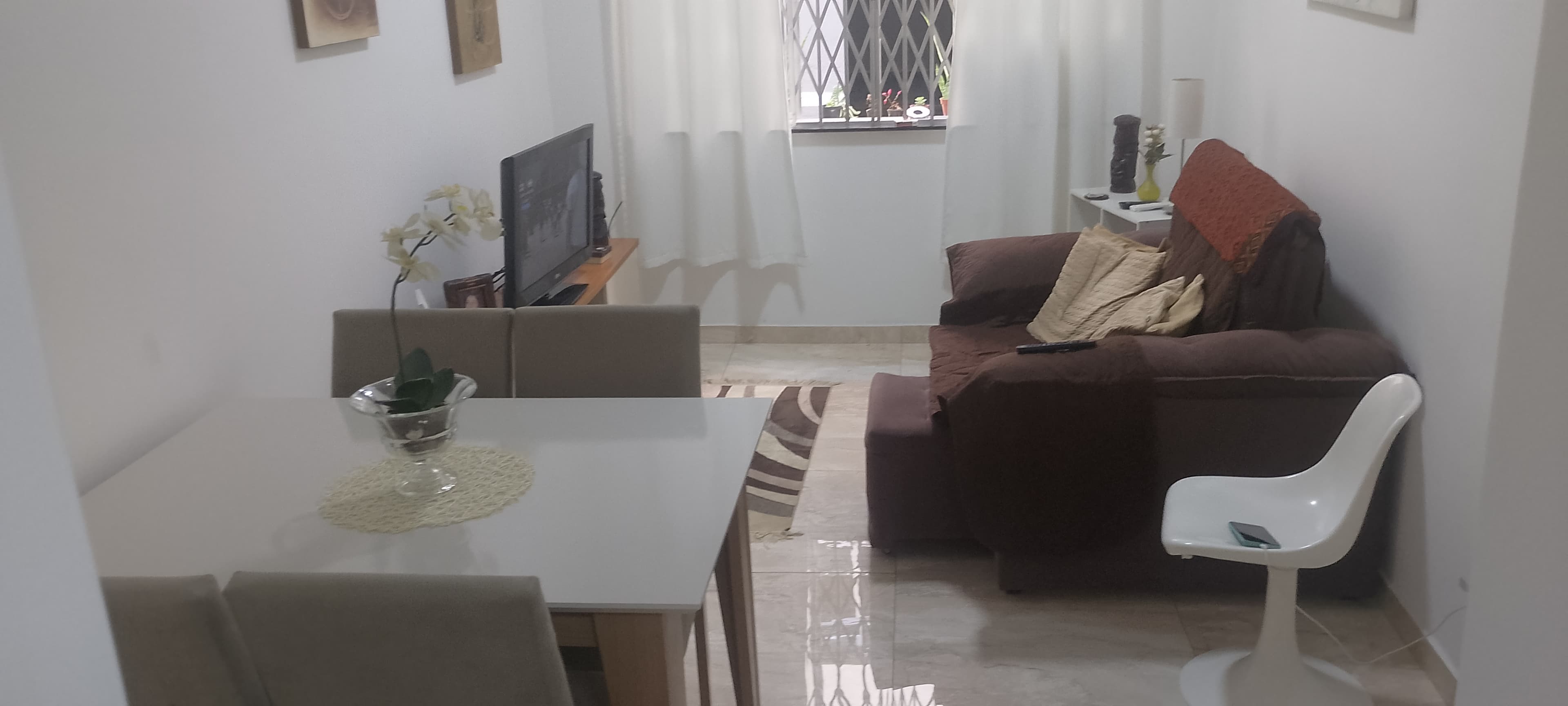 Sala de estar e jantar integrada com sofá marrom, mesa de jantar e televisão.
