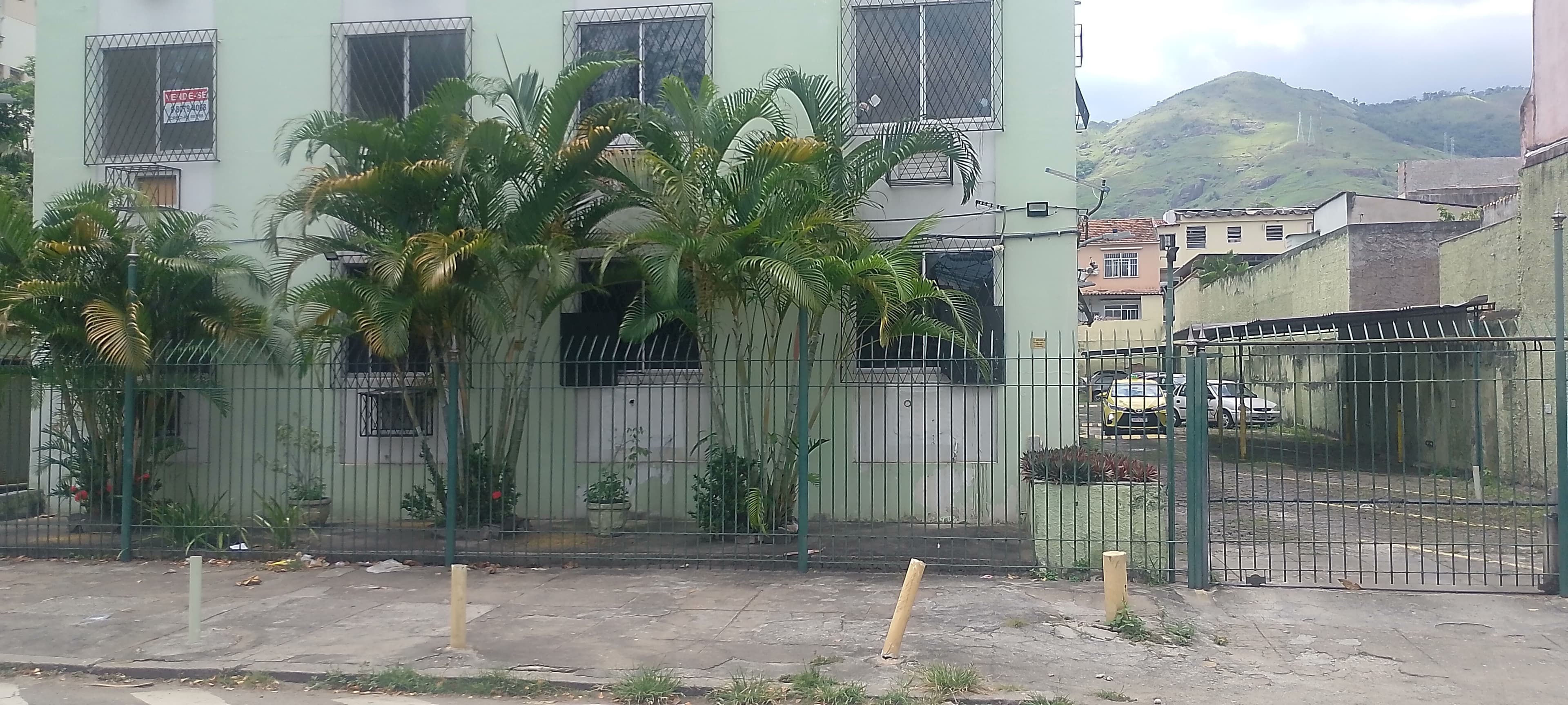 Fachada de prédio residencial com pintura clara, grades de proteção e palmeiras na frente.