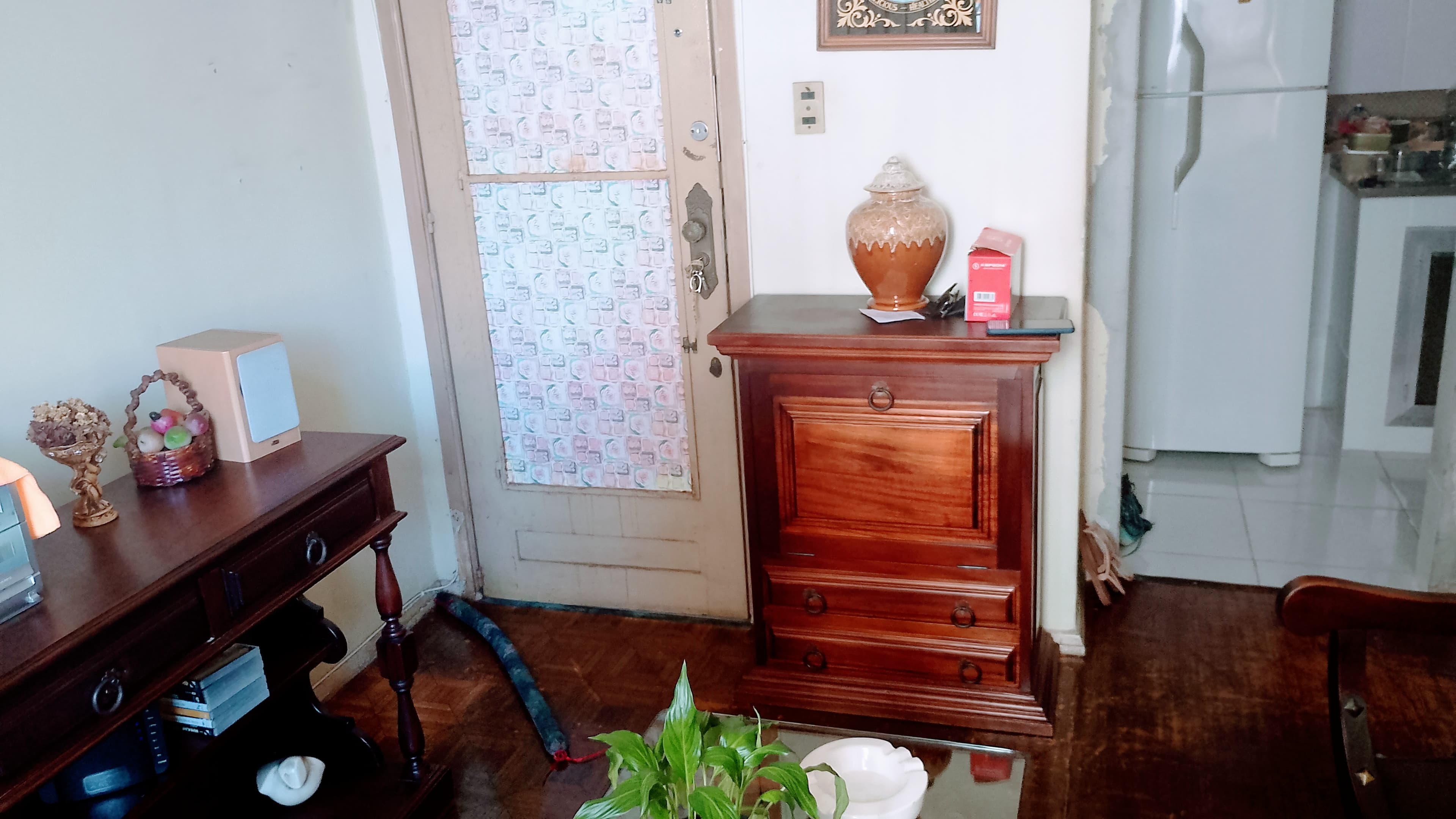 Sala com móvel de madeira estilo clássico, porta de entrada e vista parcial para cozinha ao fundo.