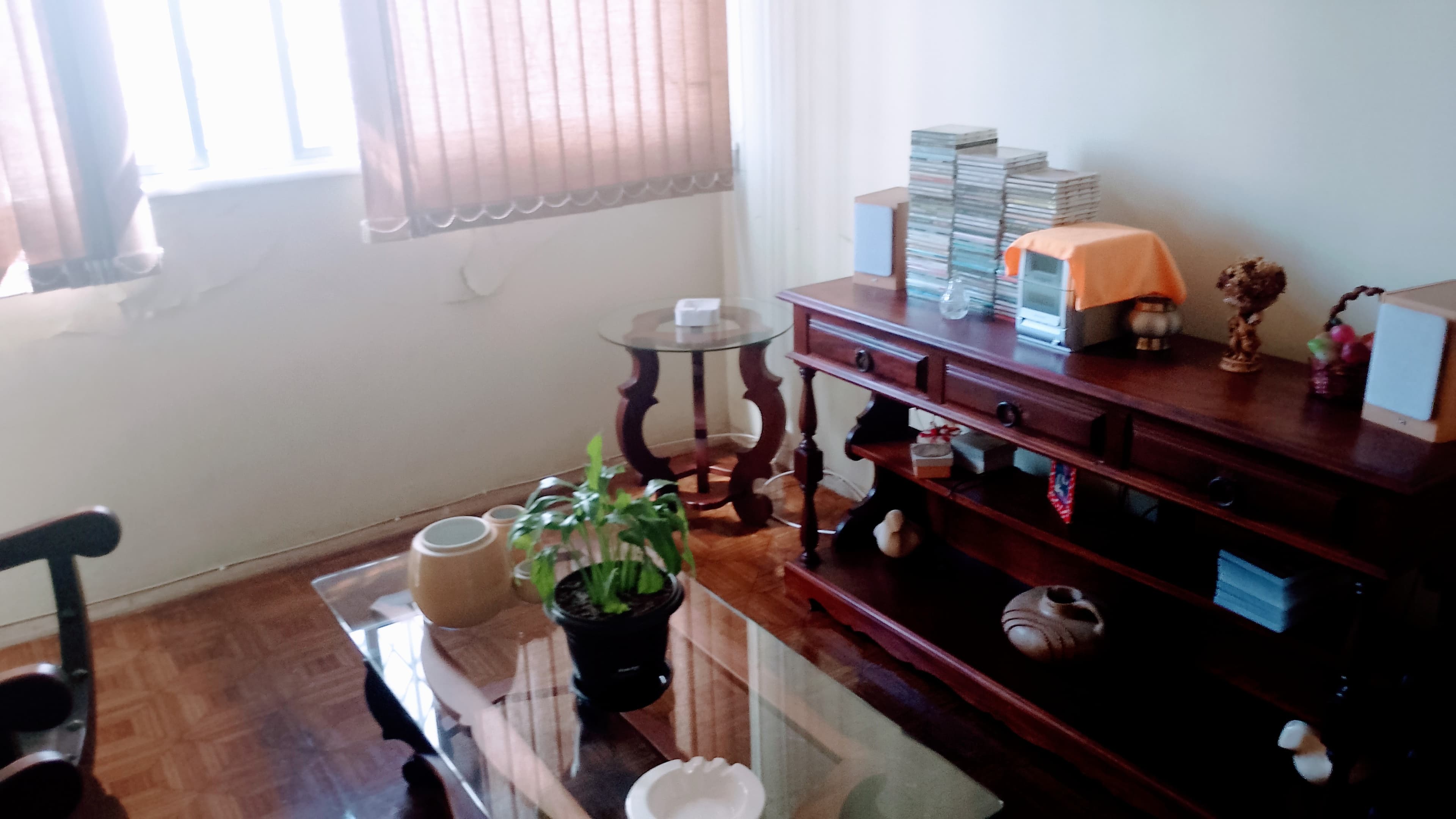 Sala com piso de madeira, mesa de centro de vidro, aparador de madeira e persiana na janela.